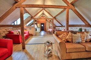 Ein geräumiges Schlafzimmer im Dachgeschoss mit hohen Decken, Holzbalken, einem roten Sofa, einem braunen Sofa und einem Essbereich mit Tisch und Stühlen.