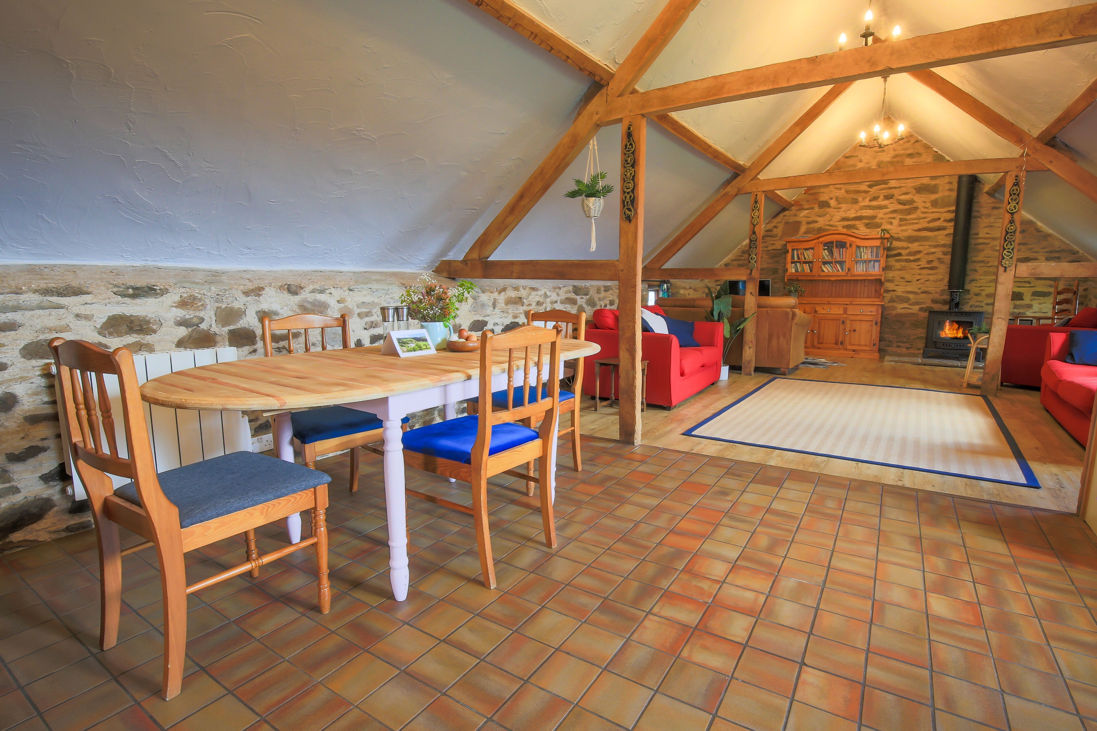 Acogedor dormitorio en el ático con una mesa de madera, sillas, un sofá rojo, chimenea y una pared de piedra.