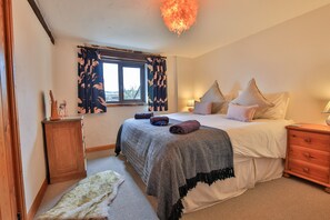 A bedroom with a bed, bedside tables, a window with curtains, a lamp, and a small cabinet. - Two Cottages, One Escape, Stunning Views (Dulverton)