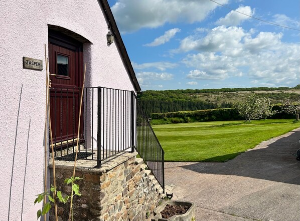 A building with a stone foundation and a red door, a stone staircase leading to a porch, and a clear view of a green field and trees in the background.