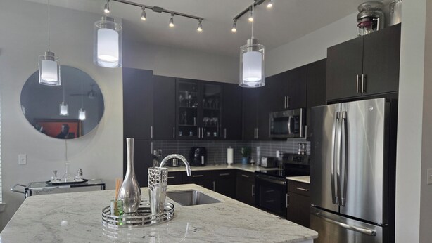 Une cuisine moderne avec des meubles de couleur sombre, des appareils en acier inoxydable et des luminaires suspendus.