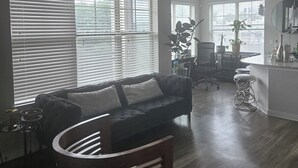 Un salon moderne avec un canapé foncé, un fauteuil en bois et un coin repas doté d’un bar.