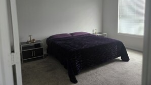 Une chambre à coucher comprenant un lit, une table de chevet, un bureau et une fenêtre avec des stores.