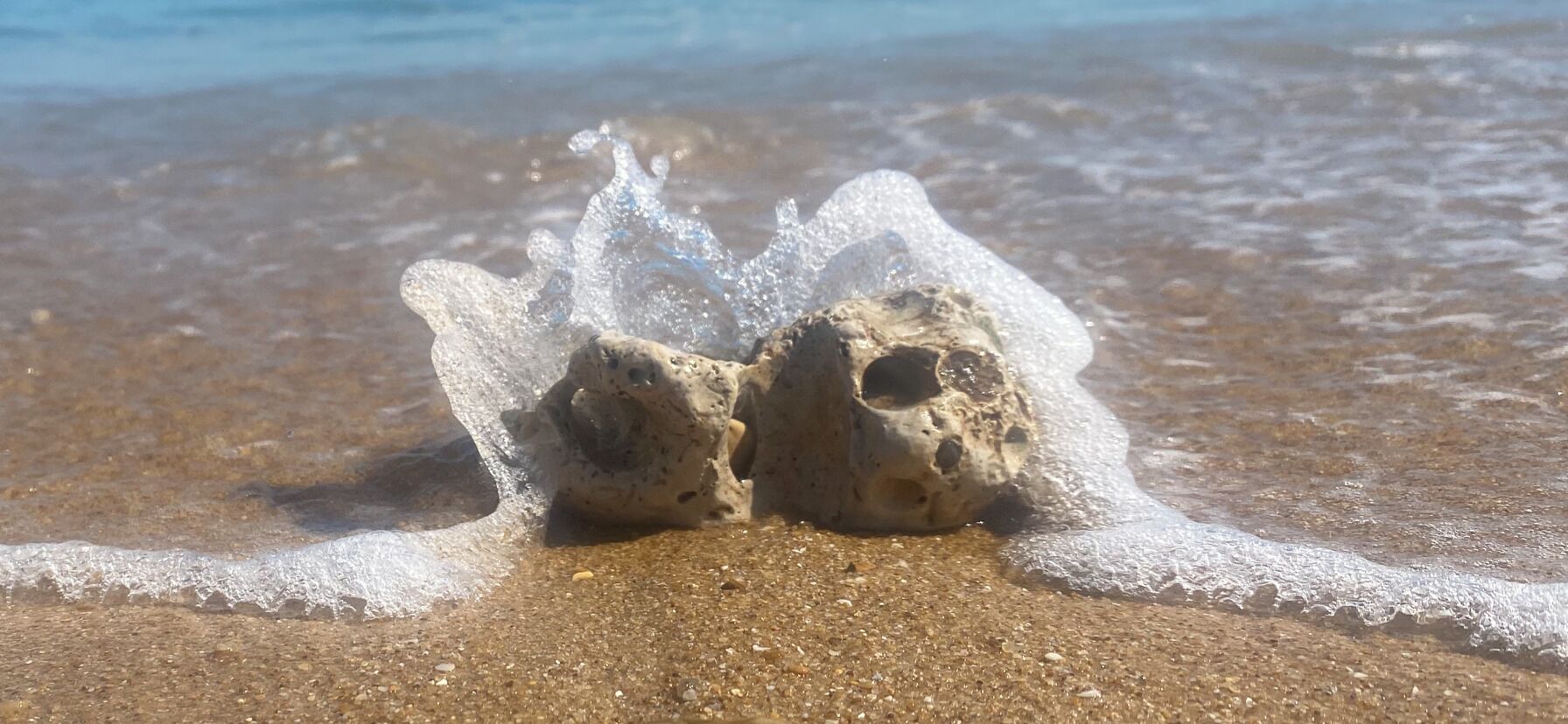 Una formación rocosa en una playa arenosa con olas rompiendo a su alrededor.