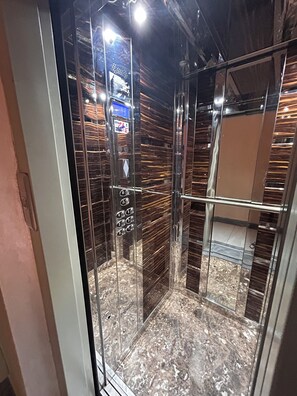 Un ascenseur à cabine vitrée doté d’un panneau de commande et d’un sol en marbre.