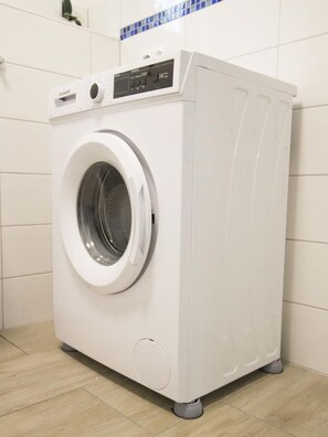 Eine weiße Frontladewaschmaschine in einem Badezimmer mit gefliesten Wänden und Holzboden.