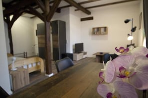 A room with a wooden dining table, a bed with a headboard, a TV, and a lamp. - NEW! Apartment Beamed room (Alsfeld)
