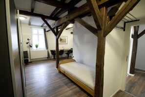 A room with a wooden ceiling, a bed, a desk, chairs, a radiator, and a window. - NEW! Apartment Beamed room (Alsfeld)