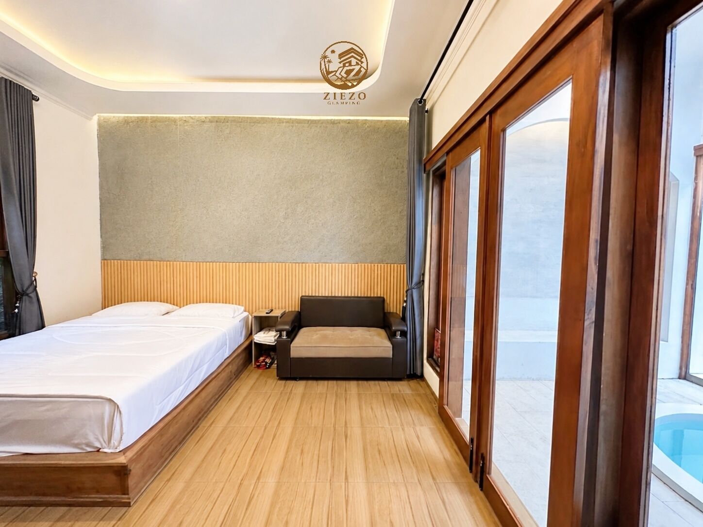 A hotel room with a bed, a sofa, a nightstand, and a large window.
