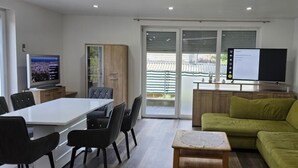Ein modernes Wohnzimmer mit Essbereich, einem Fernseher und einer Glasschiebetür zum Außenbereich.