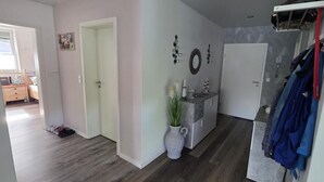 Ein Flur mit Tür, einem kleinen Schrank mit Pflanze und einem Kleiderständer mit Kleidung.