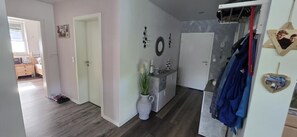 Ein Flur mit Tür, einem kleinen Schrank mit Pflanze und einem Kleiderständer mit Kleidung.