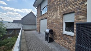 Ein Wohnhaus mit Backsteinfassade, Metallbedachung, Grill und einem Fenster mit Rollläden.