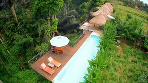 A pool area with lounge chairs and a table, surrounded by lush greenery and a thatched-roof structure. - Amara Giri Ubud Views Villas (Ubud)
