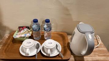 A tray with two white cups, two spoons, two bottles of water, a bowl of snacks, and a kettle.