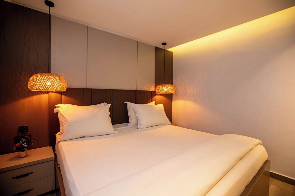Una habitación de hotel con cama, lámparas de noche, mesita de noche y estante en la pared.