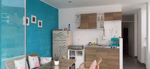 Ein kompakter Wohnbereich mit Küchenzeile, einem Essbereich mit Tisch und Stühlen sowie einer Wand in Blautönen.