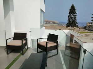 Ein Balkon mit zwei Korbstühlen und einem Glasgeländer mit Blick auf die Küste.