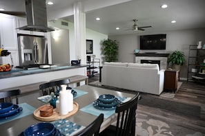 Eine moderne Küche mit Einbauherd, ein Essbereich mit Tisch für zwei Personen, ein Wohnzimmer mit Sofa und Flachbildfernseher sowie ein Deckenventilator.