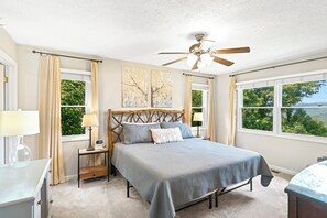 A bedroom with a bed, a nightstand, a lamp, a ceiling fan, and two windows with curtains. - Sugar on the Rocks: Mountain View, Hot Tub, Pool Table, Fire-Pit, Pet Friendly (Sugar Mountain)