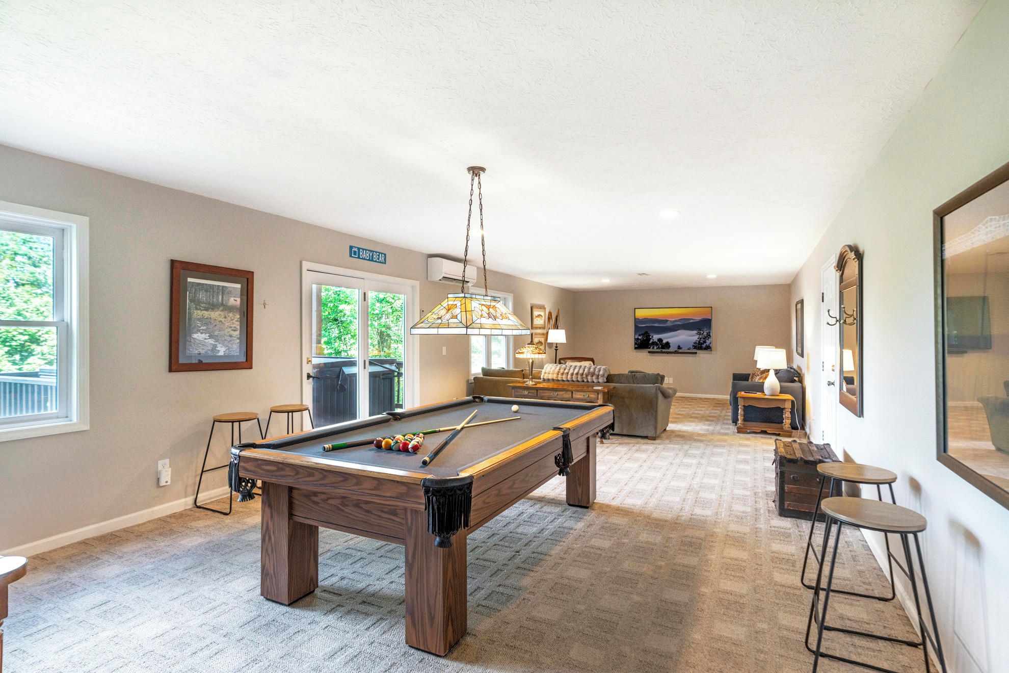 A spacious room with a pool table, a billiards rack, and a bar area with stools.