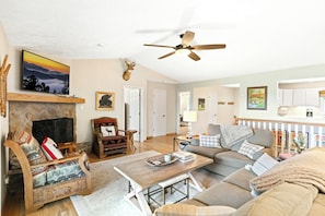A living room with a fireplace, a ceiling fan, and a view of the kitchen.