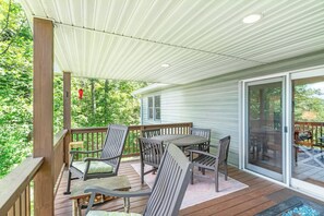 A covered deck with a table and chairs, a wooden railing, and a view of a house with a sliding glass door. - Sugar on the Rocks: Mountain View, Hot Tub, Pool Table, Fire-Pit, Pet Friendly (Sugar Mountain)