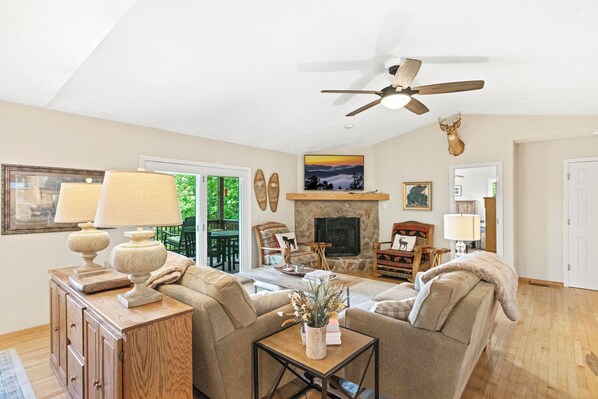 A living room with a fireplace, a ceiling fan, and a view of the outdoors through a sliding glass door. - Sugar on the Rocks: Mountain View, Hot Tub, Pool Table, Fire-Pit, Pet Friendly (Sugar Mountain)