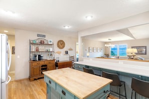 A kitchen with a wooden island, bar stools, a clock, and a view of the outdoors.