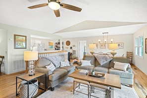 A spacious living room with a ceiling fan, a dining area with a table and chairs, and a kitchen in the background.