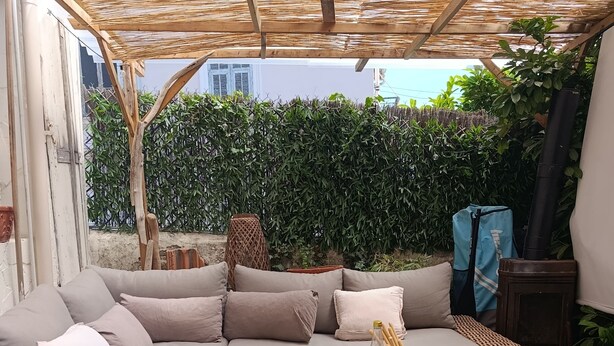 Een knus terras met een bank en rieten tafels, omringd door groen en een pergola.