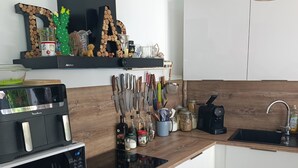 Een moderne keuken met een magnetron, fornuis en spoelbak. Er zijn houten kastjes, een zwart schap met decoratieve voorwerpen en een houten achterwand.