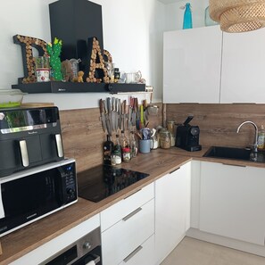 A modern kitchen with a microwave, stove, and sink. There are wooden cabinets, a black shelf with decorative items, and a wooden backsplash. - 3-bedroom house in Nice, a stone's throw from the beach (Nice)