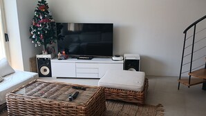 Een moderne woonkamer met een flatscreen televisie, rieten meubels, een kerstboom en een trap.