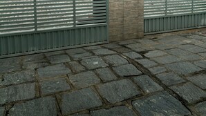 Een geplaveid gebied met een metalen hek, een bakstenen muur en een gebouw op de achtergrond.