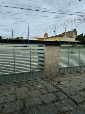 Ein gepflasterter Bereich mit einem Metallzaun, einer Ziegelwand und einem Gebäude im Hintergrund.
