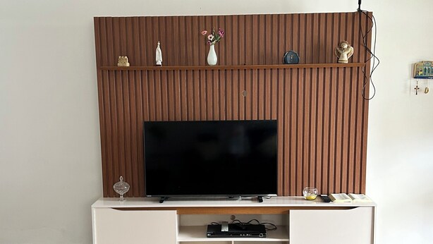 Een woonkamer met een flatscreen televisie, houten paneelwand, een witte meubelset en een kroonluchter.
