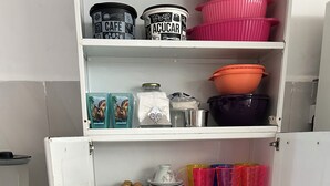 Een keuken met een witte koelkast, een koffiezetapparaat en verschillende keukengerei en bakjes op planken.