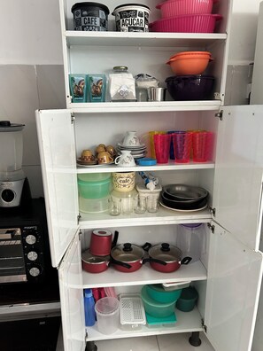 Eine Küche mit einem weißen Kühlschrank, einer Kaffeemaschine sowie verschiedenen Küchenutensilien und Behältern auf Regalen.