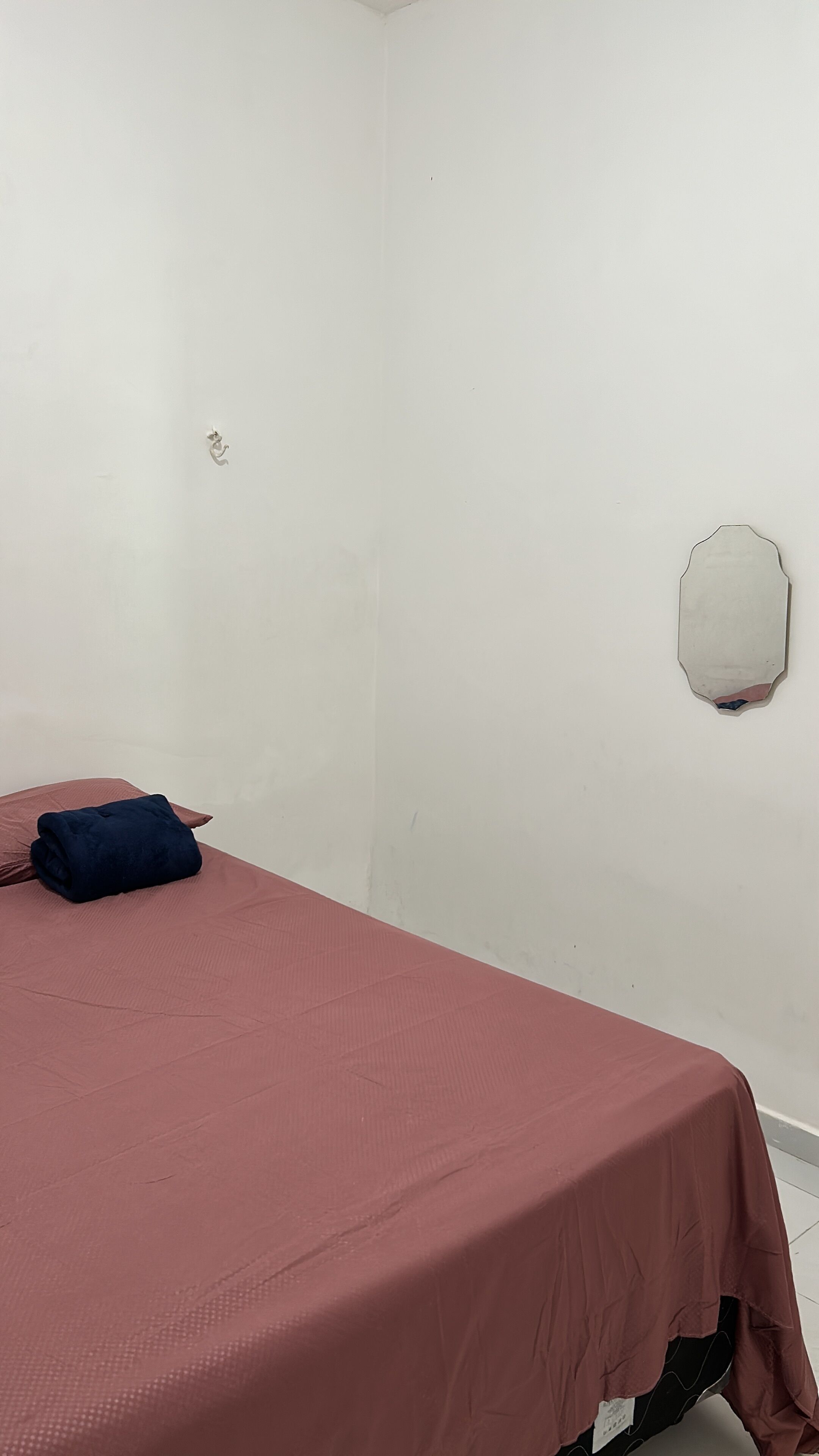 Una habitación con una cama individual, un pequeño agujero en la pared y una colcha roja.
