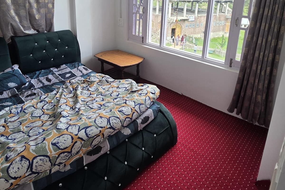 Quarto com cama, ventilador de teto, janela e uma pequena mesa.