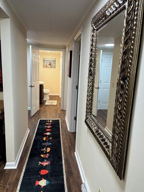 Un couloir avec un tapis noir orné de motifs de poissons colorés, un grand miroir décoratif et une porte donnant sur une salle de bain.