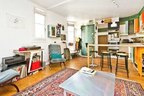 Ein gemütliches Wohnzimmer mit Couchtisch, Bücherregal, Sessel und einem gemusterten Teppich.