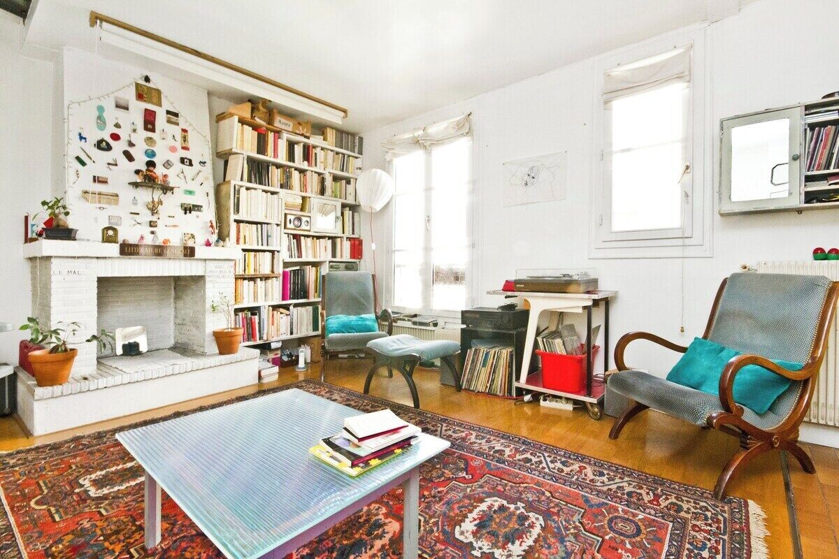 Un salon avec une cheminée, des étagères à livres, une table basse et un tapis à motifs.
