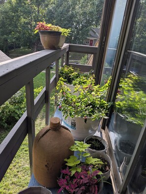 A balcony with potted plants, a burlap sack, and a window.