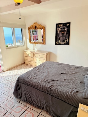 Ein Schlafzimmer mit Bett, Schminktisch, Spiegel, Kunstwerken und Meerblick.