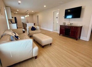 Ein Wohnzimmer mit Sofa, Hocker und einem an der Wand befestigten Flachbildfernseher.