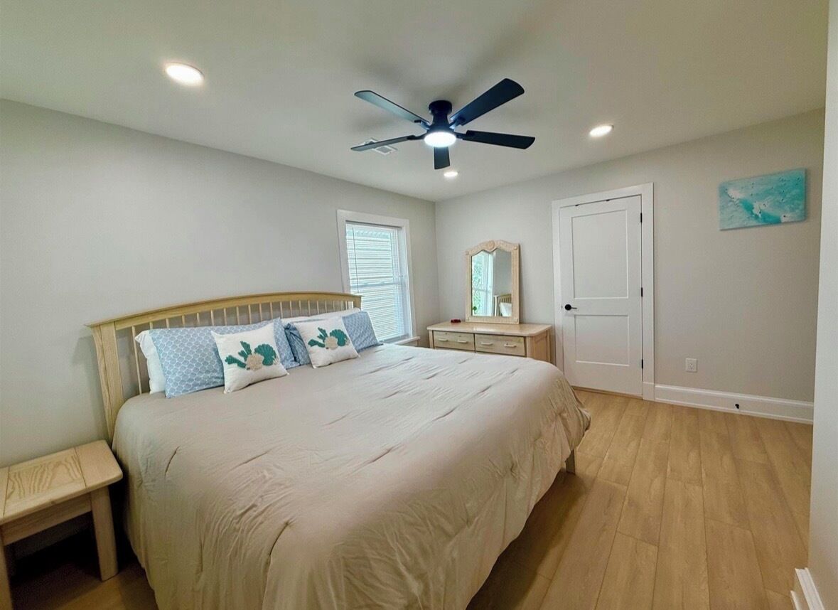 A bedroom with a bed, bedside table, ceiling fan, and a door.