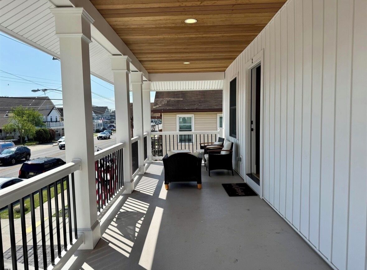 A covered porch with a railing, a bench, and a door leading to a room.
