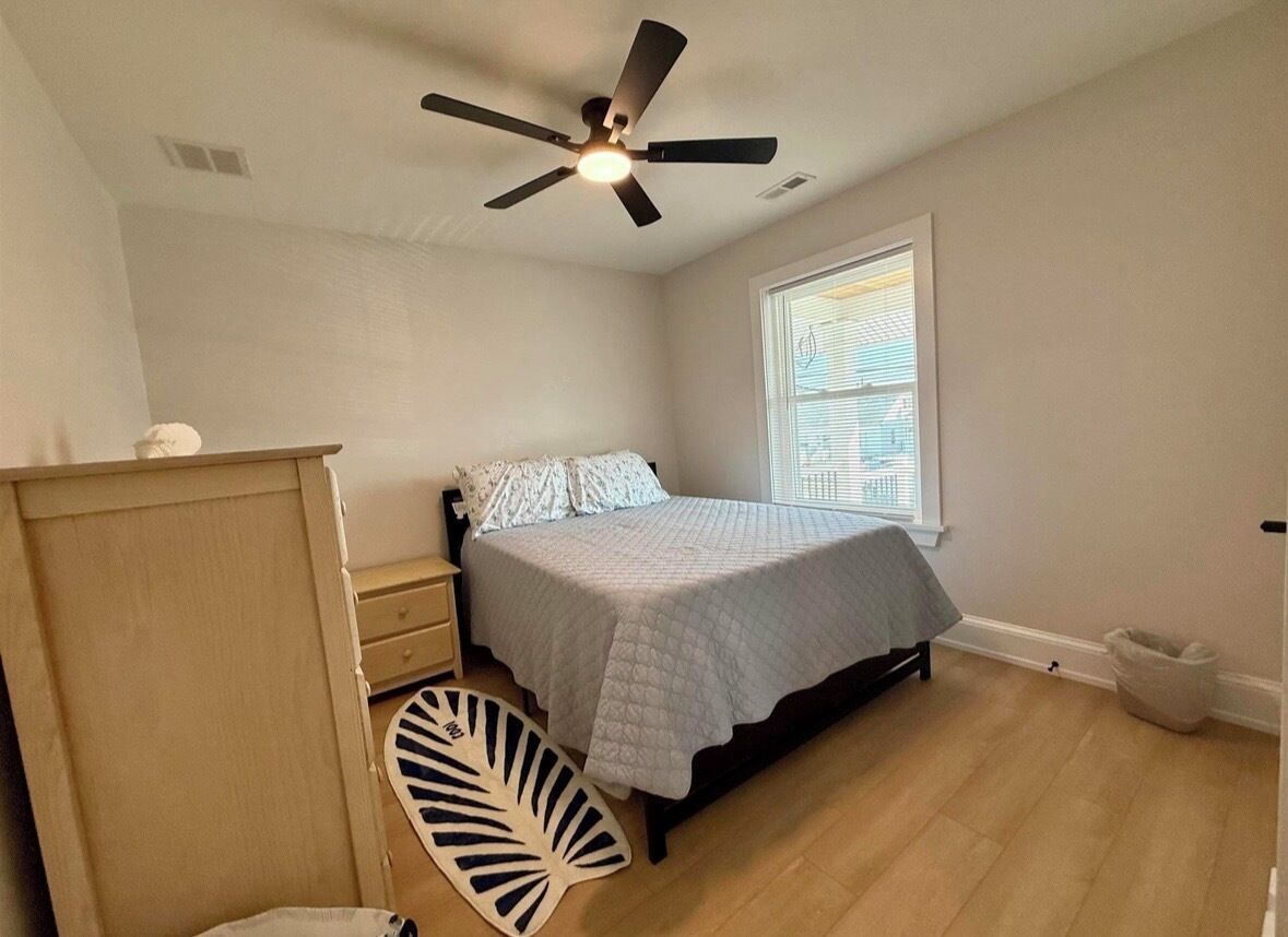 Un dormitorio con cama, ventilador de techo, ventana y cómoda de madera.